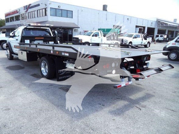 Ram 5500 SLT tow truck in lot with flatbed trailer and back-view, multiple white service trucks in background.