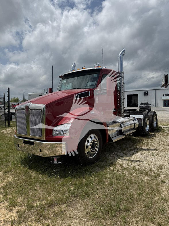 Kenworth T880 tractor in a red color, front grille, large chrome exhaust stacks, dual rear axles, chrome fuel tanks, daytime with cloudy sky.