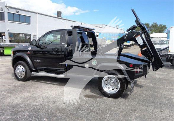 Ram 4500 SLT tow truck with black cab and dual rear wheels, hydraulic tilt-bed in raised position, chrome wheels, side steps.