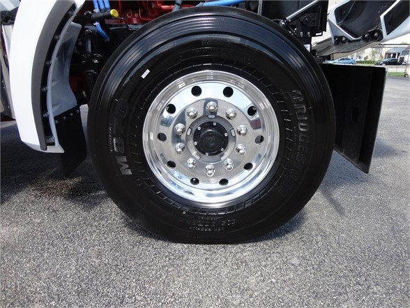 Kenworth W990 wheel and tire assembly showing polished steel wheel with multiple lug nuts and Bridgestone or similar tire, front fender and undercarriage components visible.