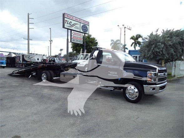 Flatbed tow truck in a dealership lot with TLC Truck Sales Center sign in background.