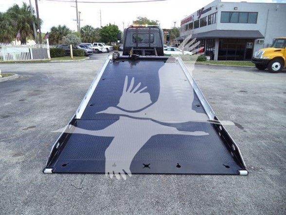 Tow truck tilt bed with diamond plate surface and built-in ramps, viewed from tail of flatbed.