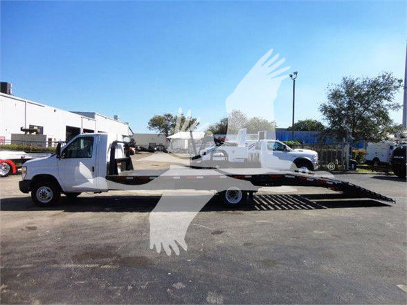 2011 Ford E450 flatbed tow truck with ramped loading bed and extended flatbed, side view, dealership yard in background.