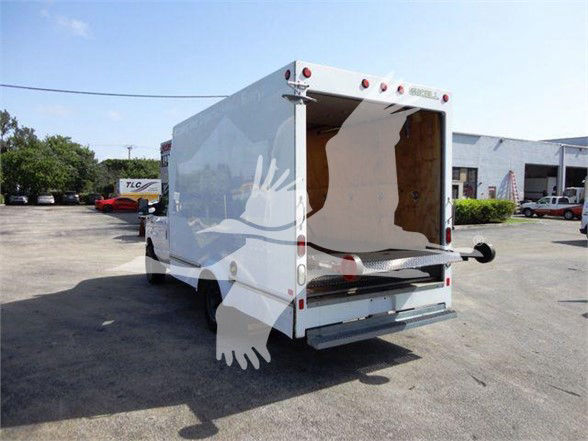 Ford E-350 box truck rear view with open cargo area, hitch, and taillights. No visible branding text legible on the truck itself from this angle.