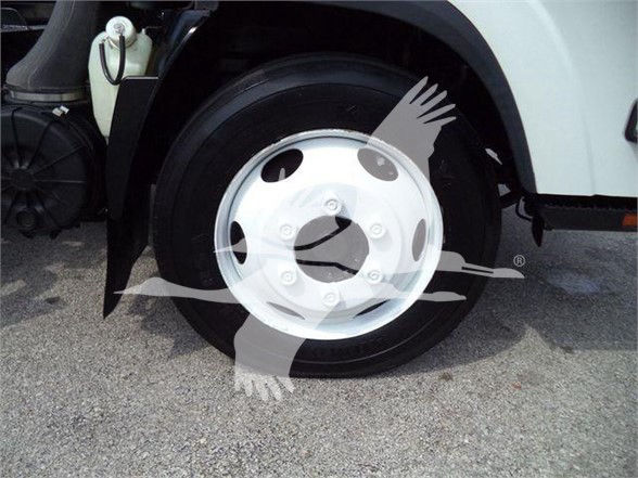 Isuzu NRR front wheel with white metal hubcap and black tire, part of a white truck, with fluid reservoir visible in background.