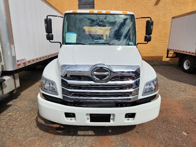 Front view of white 2025 Hino L6 cab chassis truck with large chrome grille and Hino emblem, headlights, and bumper.