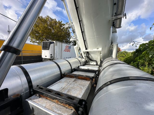 Warehouse vacuum truck body with large cylindrical tanks and hydraulic arm, side view showing metal piping and a white refrigeration unit in background.