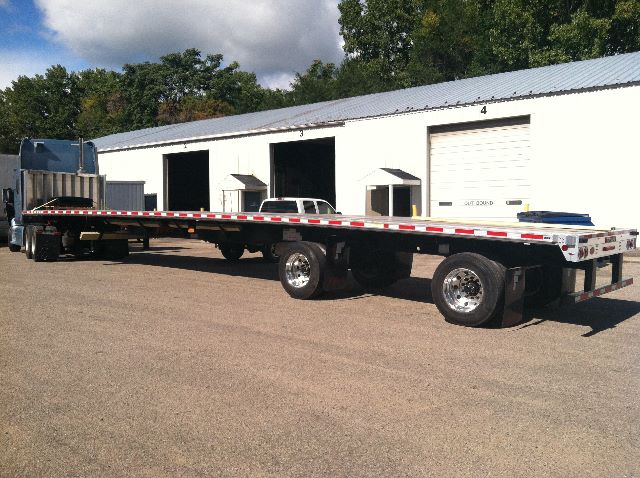 Flatbed trailer with long orange and white reflective side rails, dual rear axles, Fontaine 53' x 102" display in a yard.