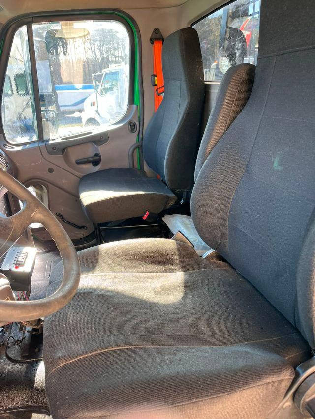 Cab interior of a Freightliner M2-106 truck showing driver and passenger seats, steering wheel, and door panel.