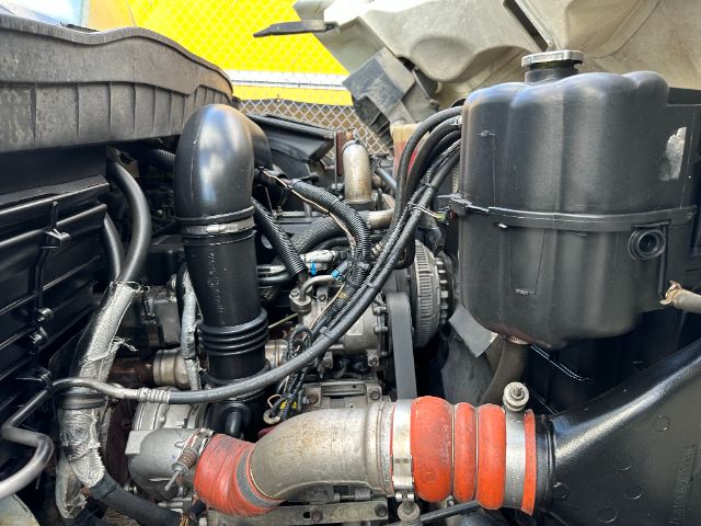 Truck engine bay showing air intake hose, coolant reservoir, and red silicone hose connected to a turbo with surrounding hoses and components.