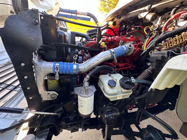 Front engine bay of a 2014 Freightliner M2 showing radiator, coolant reservoir, power steering lines, and various hoses and hydraulic components.