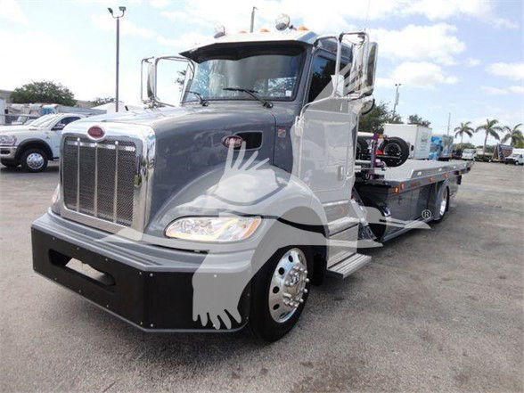 Peterbilt 337 tow truck in gray with chrome grille and sleeper cab, front view in dealership lot.