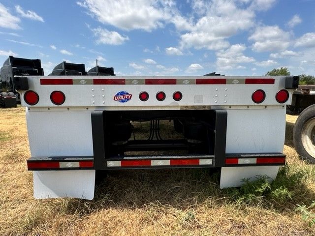 Flatbed trailer rear view showing Utility logo, red circular taillights, and black reinforced frame beneath white mud flaps.