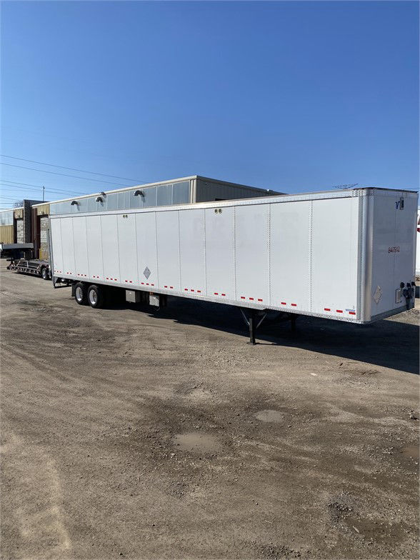 A white Vanguard dry van trailer with two axles and landing gear, parked on a gravel lot under a clear blue sky.