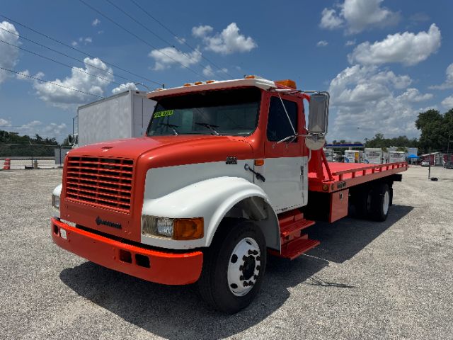 1999 International 4700 DT 466E tow truck with red and white cab, long flatbed, dual rear wheels, blue sky background.