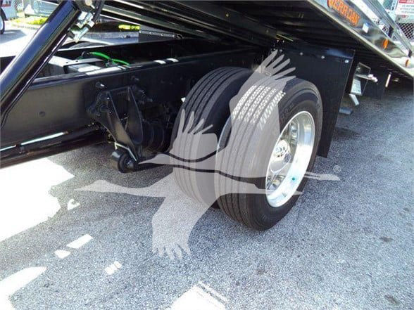 Truck rear axle and wheel area visible on a tow truck chassis with black frame and chrome wheel, hydraulic lift components nearby.