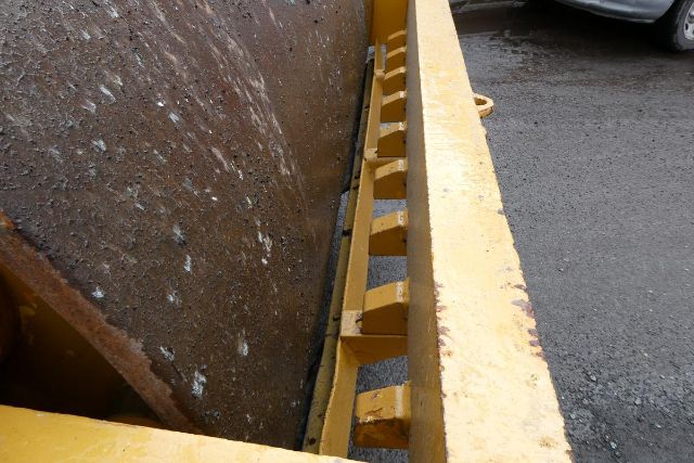 Close-up of a yellow construction machine edge with a rusted steel plate and evenly spaced brackets along the side.