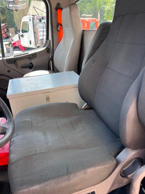 Truck cab interior showing two seats and metal storage box between seats; window and door panel visible; Freightliner M2 cab and chassis used vehicle.