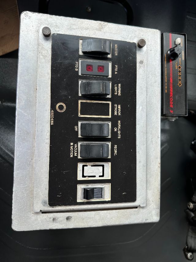 Panel with labeled switches on a Freightliner M2 dash: PTO, WARNINGS LIGHTS, MIRROR STORER? ON, WORK LIGHTS, VACUUM INFOR? RECH? Off lever, and a two-display display; metal enclosure.