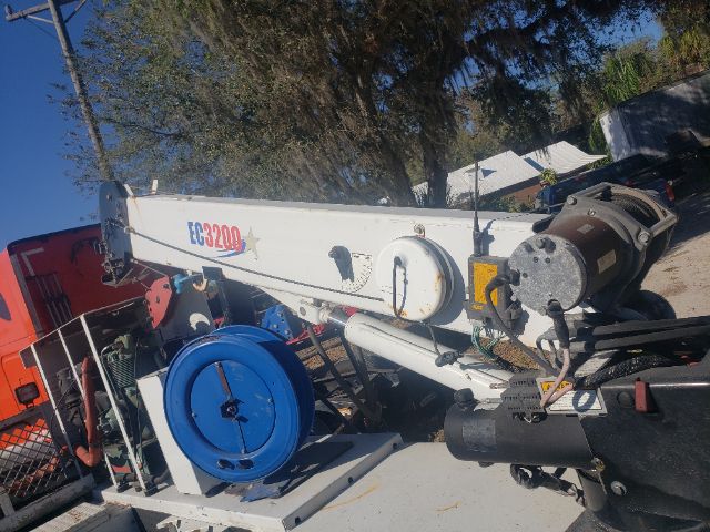 Ford F550 truck body with a long white boom labeled EC3200, blue hose reel, and various hydraulic components in an outdoor yard.