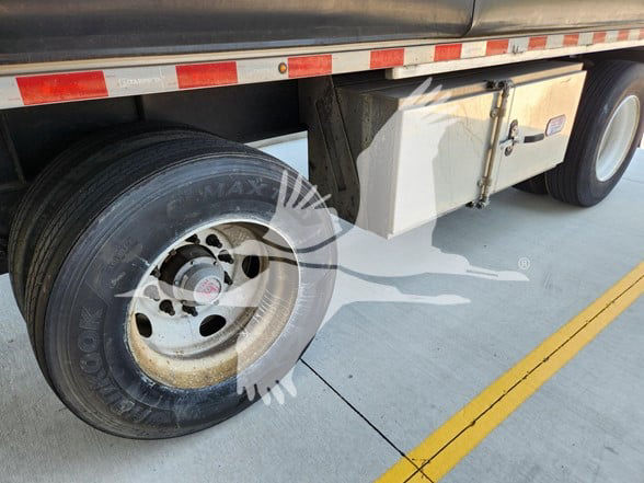 Truck trailer wheel well showing dual rear tires and a storage box mounted between the wheels. Visible text on tire and metal components.