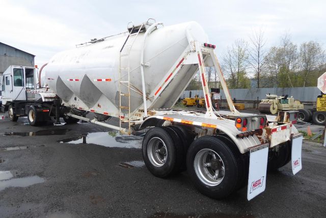 Rear-right view of a white Fruehauf pneumatic dry bulk trailer with cylindrical tank, dual rear axles, and white mud flaps.