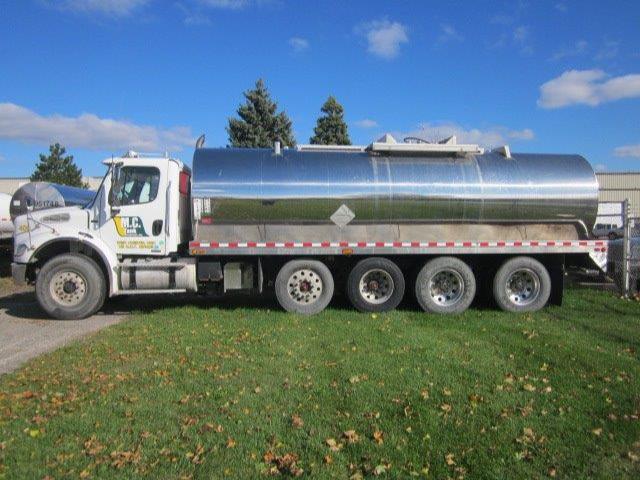 Tank trailer with a white cab and a large polished stainless steel cylindrical tank. Flatbed or support structure under tank with three axles at rear. Visible text on cab door area.