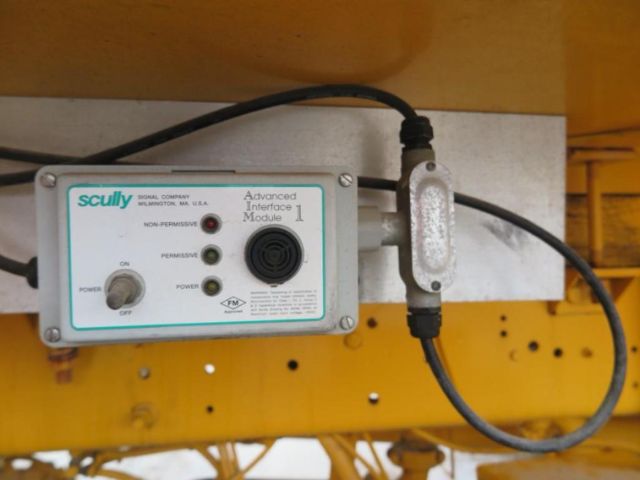 Scully Advanced Interface Module control unit with two indicator LEDs, labeled OFF/ON, on a yellow metal surface with wiring, appears to be part of a utility vehicle.