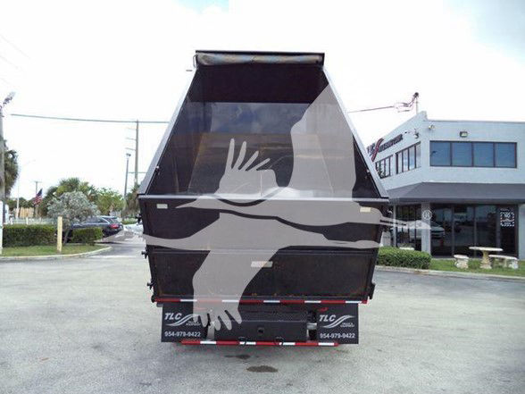 Back view of a Ford E-450 dump truck, black dump bed raised, with TLC logo and contact numbers on bumper.