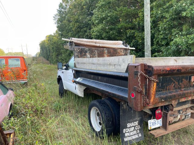 Truck bed with rusted dump trailer attached, white Ford F-450 in-service, chain on tailgate, 'SHADE EQUIP. CO.' small text on rear bumper, license plate visible, overgrown grass.