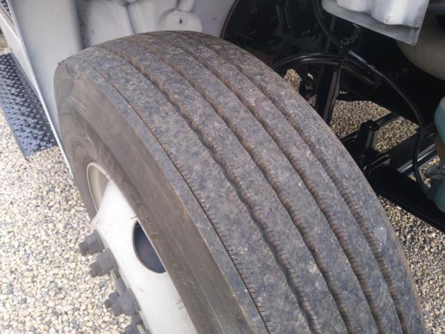 Wheel/tire on Freightliner M2 front steering with dual axles and visible tread wear; part of suspension and chassis visible.