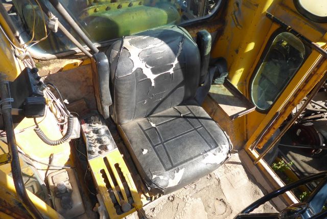 Cab interior of a Caterpillar 16G showing worn seat with tears, yellow metal framework, control levers and wiring in view.