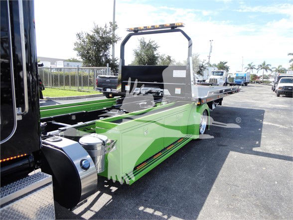 Green Peterbilt 337 tow truck flatbed with black rollover bar and yellow light bar in a parking lot.