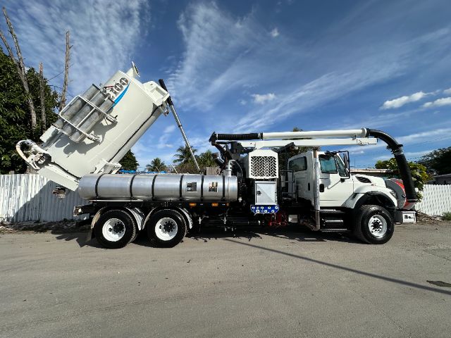 2013 International 7500 vacuum truck with rear dump body and mounted vacuum system, white cab, large cylindrical tanks, and a long articulated hose arm.