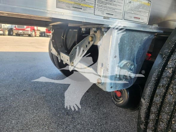 Flatbed trailer wheel and suspension visible under trailer with label stickers on frame