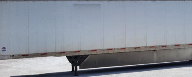 Trailer side with landing gear visible, utility trailer with white side panel and reflective tape along bottom edge.