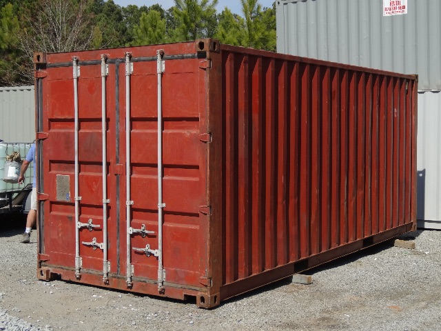 Red cargo container with metal doors and vertical ribs, placed on small concrete blocks outdoors.