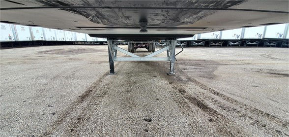 Underneath view of a Vanguard MAXCUBE dry van trailer parking area showing landing gear and underside of trailer with gravel lot.