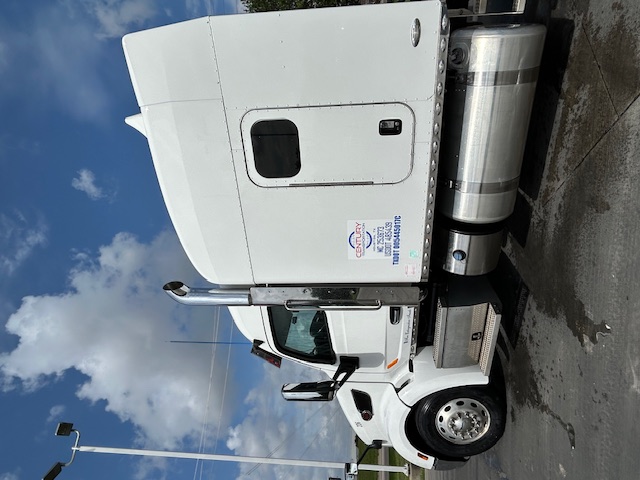 Peterbilt 579 conventional sleeper truck side view with white exterior, large chrome exhaust stack, fuel tanks, and side door window.