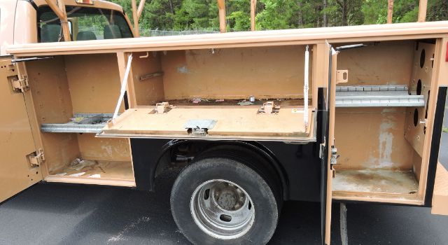 Open utility bed compartments on a 2016 Ford F350 Crew Cab utility truck showing storage shelves and empty tool bins.