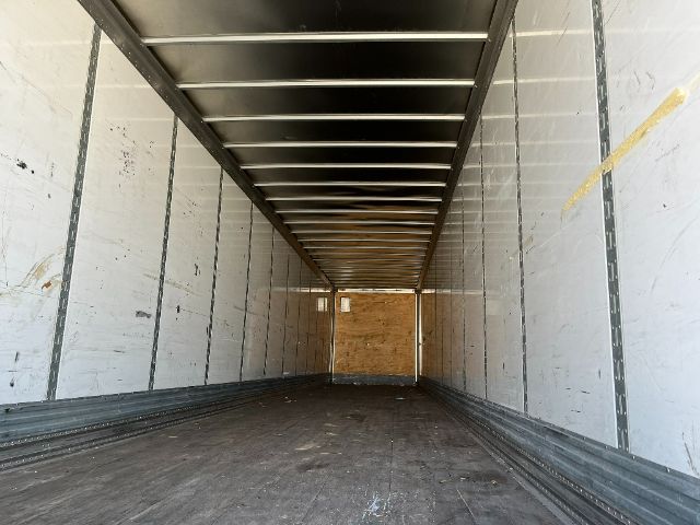 Interior view of an empty trailer cargo area with metal sidewalls, overhead support rails, and wood rear wall.