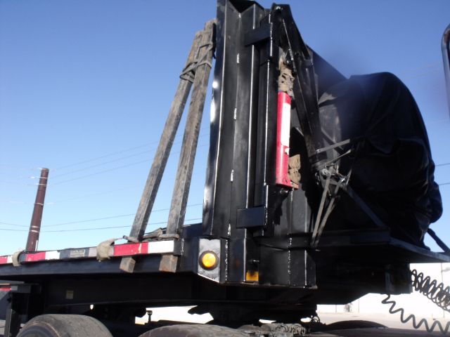 Flatbed expandable trailer with a raised teleportable mechanism and safety reflectors, black metal frame, and cover in the rear area.