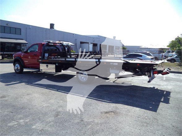 Ram 5500 tow truck with flatbed, side view showing red cab and long flatbed trailer.