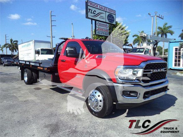 Ram tow truck with flatbed in red color, RAM grille, TLC Truck & Equipment watermark. Visible text includes TLC signs in background and RAM emblem on grille.