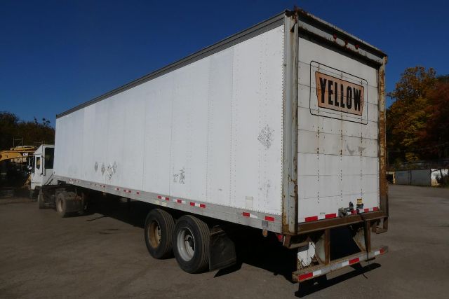 FruehaufFBHLP trailer showing rear with Yellow sign and triple-axle configuration. Side view shows white box trailer with reflective tape and landing gear.