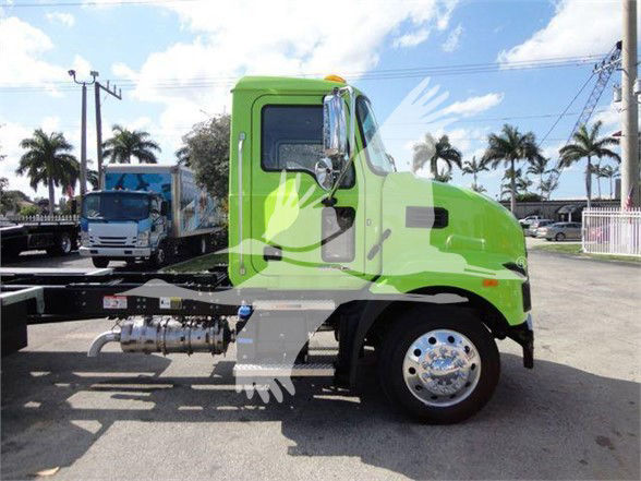 Green 2025 Mack MD6 cab facing left showing side exhaust and wheel, tow truck chassis with chrome hubcap visible.