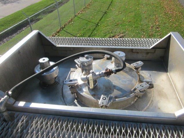 Tank truck top view showing circular access hatch with hoses and fittings in a metal compartment.