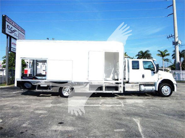 Tow truck in white, cab with large rectangular living quarters on trailer, side door open, wheel wells, rear ramp/dock area visible.