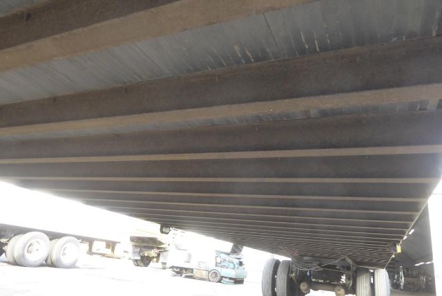 Trailer underside view showing steel cross members and wheel axles with tires visible at far end.