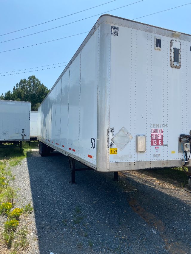 Trailer side and front of a white 2015 Wabash Duraplate trailer with support legs, caution sign, and small square access panel showing various stickers and numbers.
